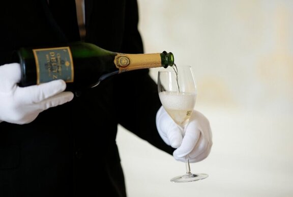 Sommelier pouring a glass of champagne, wearing white gloves.