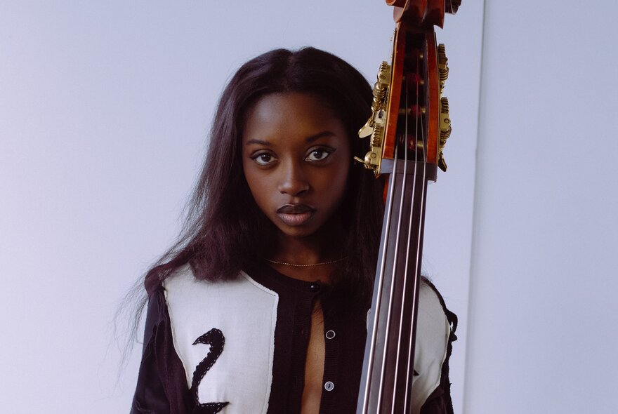 Jazz musician, Amy Gadiaga, wearing a black and white bomber jacket and posing behind the neck of a double base.