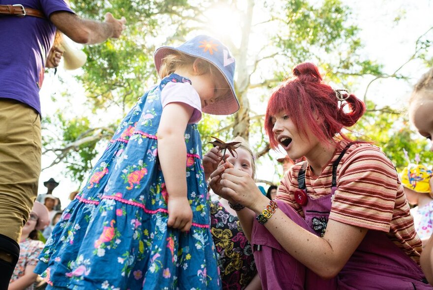 Young children and performers playing under trees.