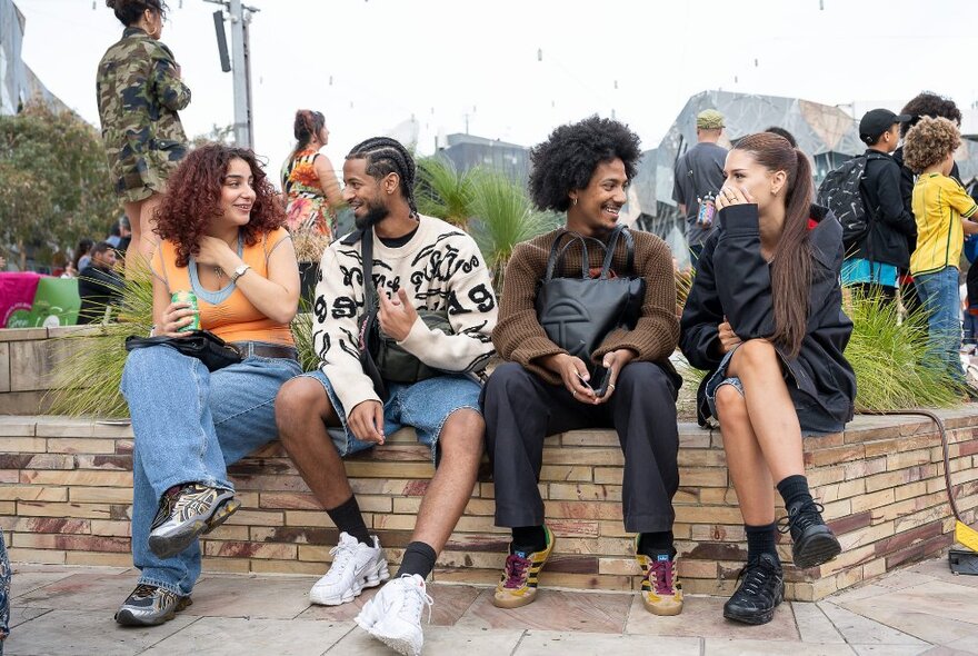 Four young adults sitting on a bench seat at Fed Square, laughing and interacting.