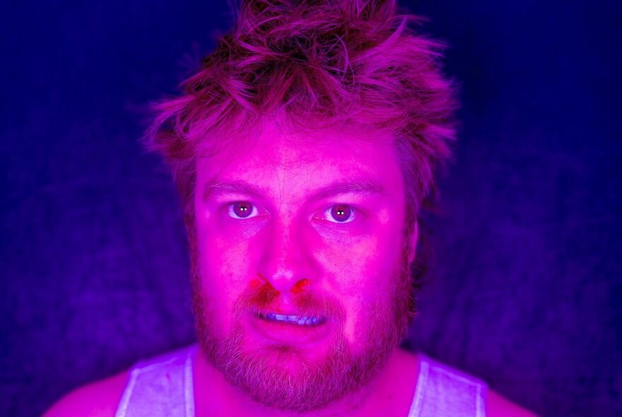 Bright pink/purple image of man with red hair and beard, wearing a singlet.