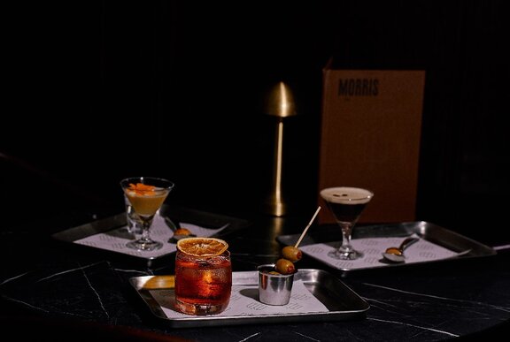 A dark and moody collection of mini cocktails with paired snacks, presented on small trays on a black marble table