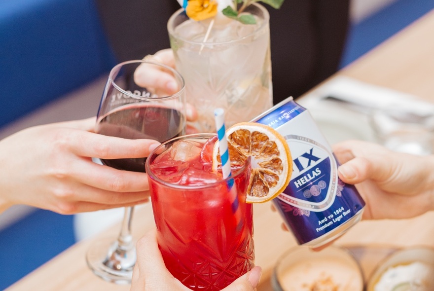 Four people clinking their drinks of wine, beer, and cocktails. 