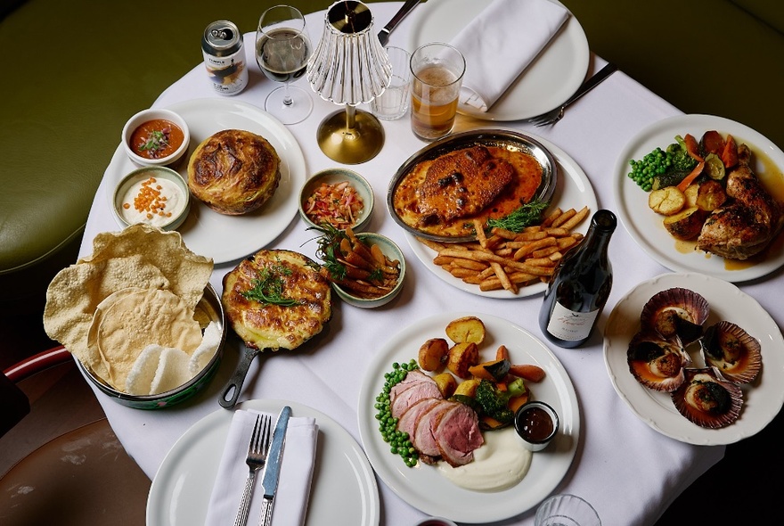 A selection of pub and Indian-style dishes displayed on a round table with a white tablecloth, seen from above.