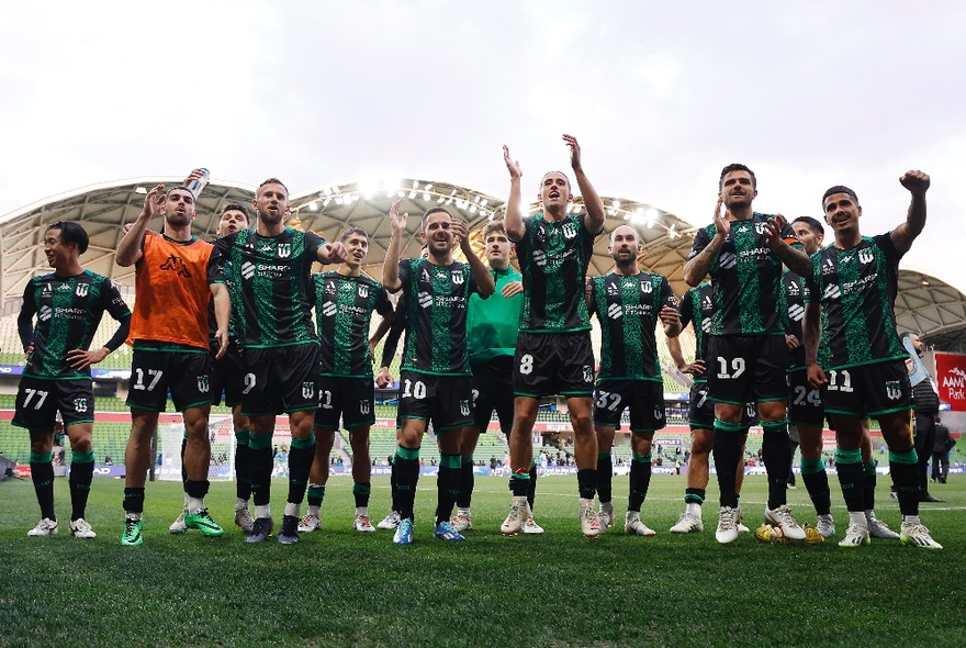 The Western United men's football team on the pitch, cheering, crowds in the stadium seats behind them.