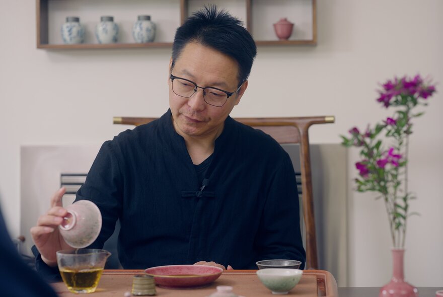 Tea Master, Merrick Chen, pouring tea from a small bowl into a glass beaker.