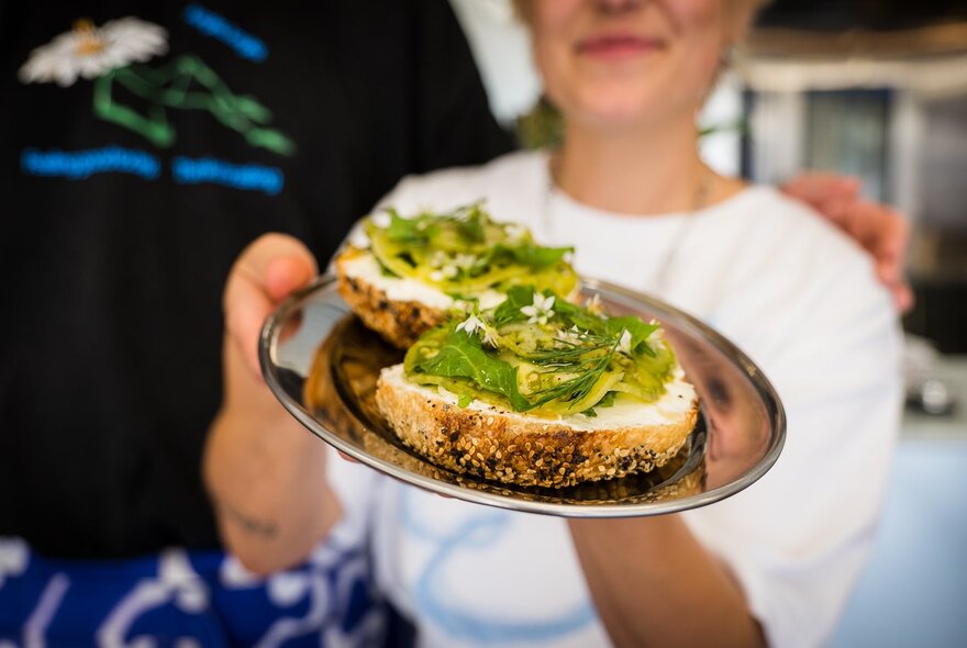 A stallholder holding a silver tray of avocado on sesame-seed bread.