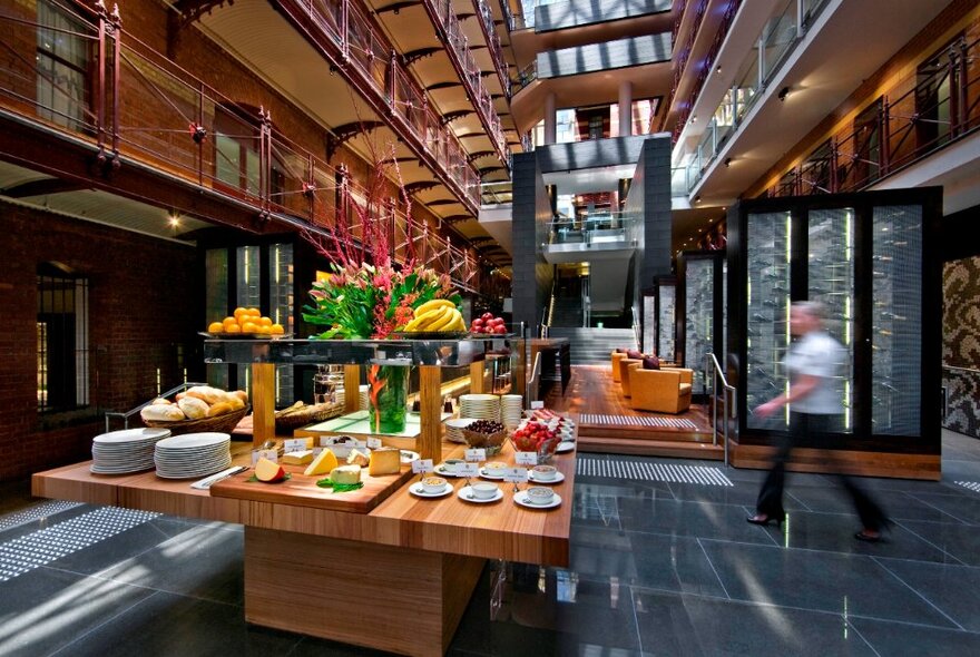 Restaurant wooden serving table in the centre of a hotel foyer overlooked by mezzanine walkways.