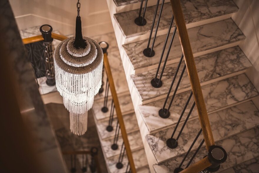 Chandelier hanging in a stairwell next to marble staircase.