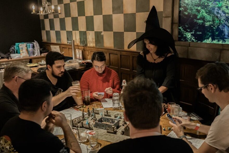 A group of friends playing the board game dungeons and dragons at Fortress Tavern Melbourne, with a Dungeon Master dressed in a witch's costume leading the game.