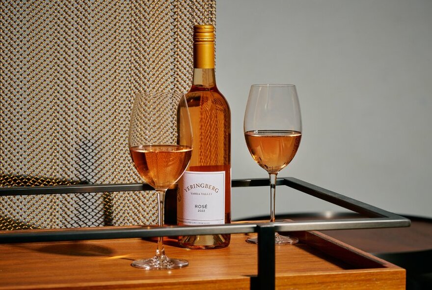 Wine bottle and two half-filled glasses on wooden and metal  bar.