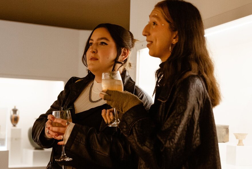 Two people inside a museum at a social event, each holding a glass of wine.