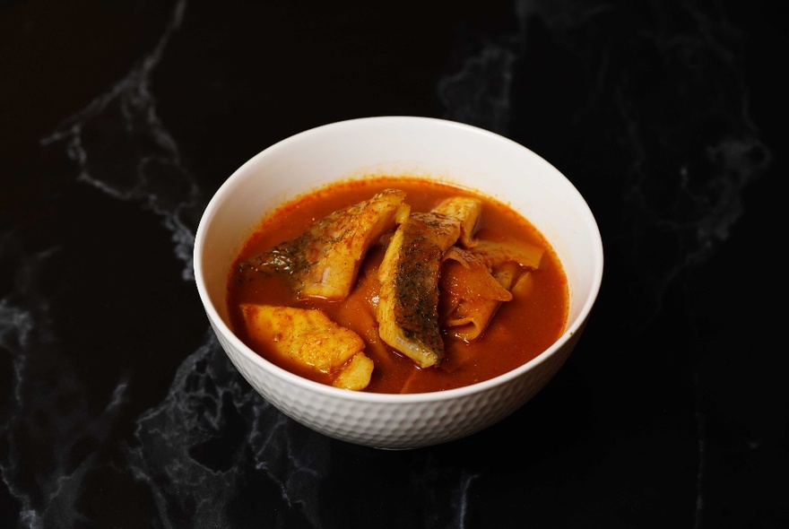 A bowl of sour fish curry on a dark table top.