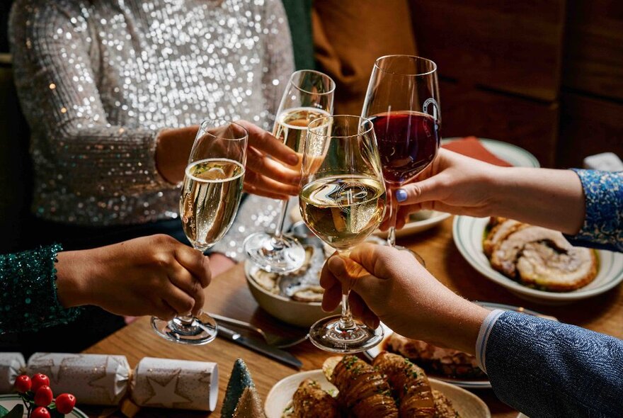 Four hands bringing four glasses of wine together in a toast.