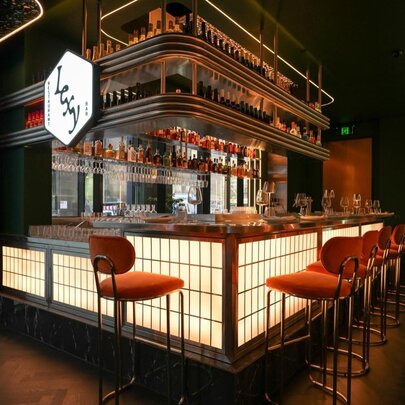 Restaurant's bar area with Asian-inspired decor, illuminated screen detail, red stools and wooden shelving.