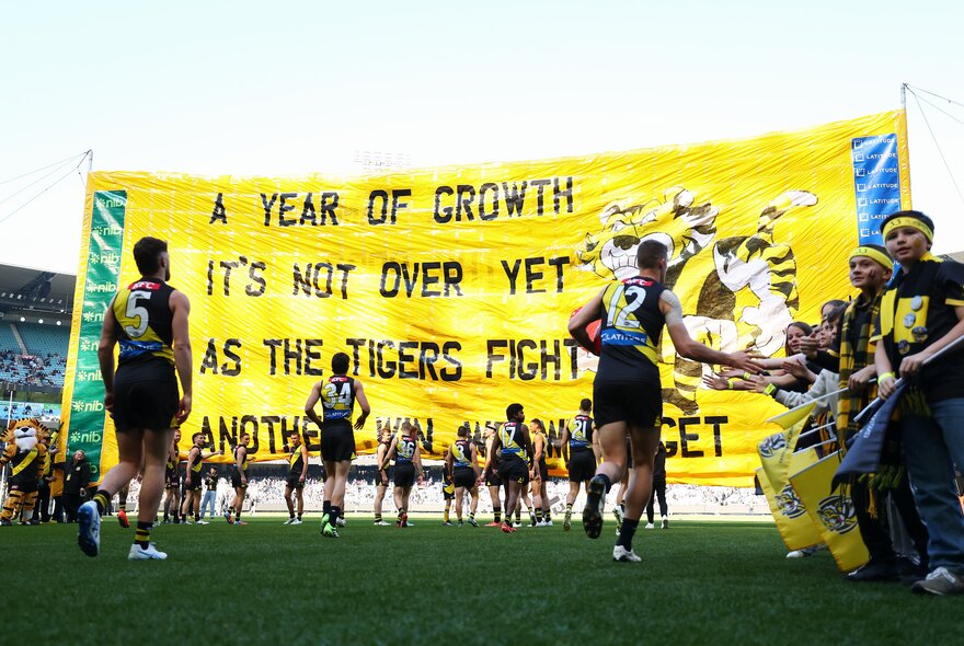 Richmond AFL football team running through a huge yellow flag.