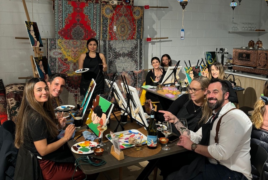 A group of people at a Paint and Sip class, learning to paint on canvas with acrylics while enjoying a glass of wine.