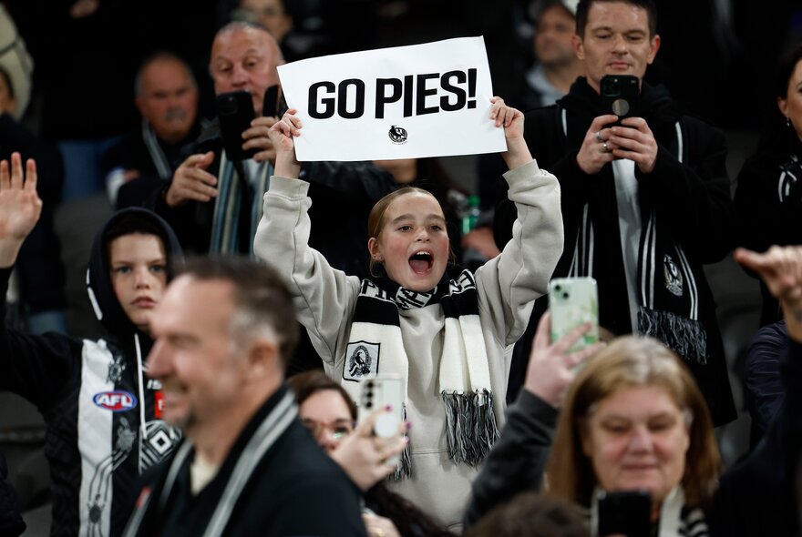 A crown at the football and a young girl holding a sign saying GO PIES.