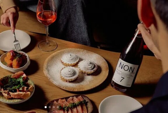 Hand holding a bottle of wine next to plates of food on a table.