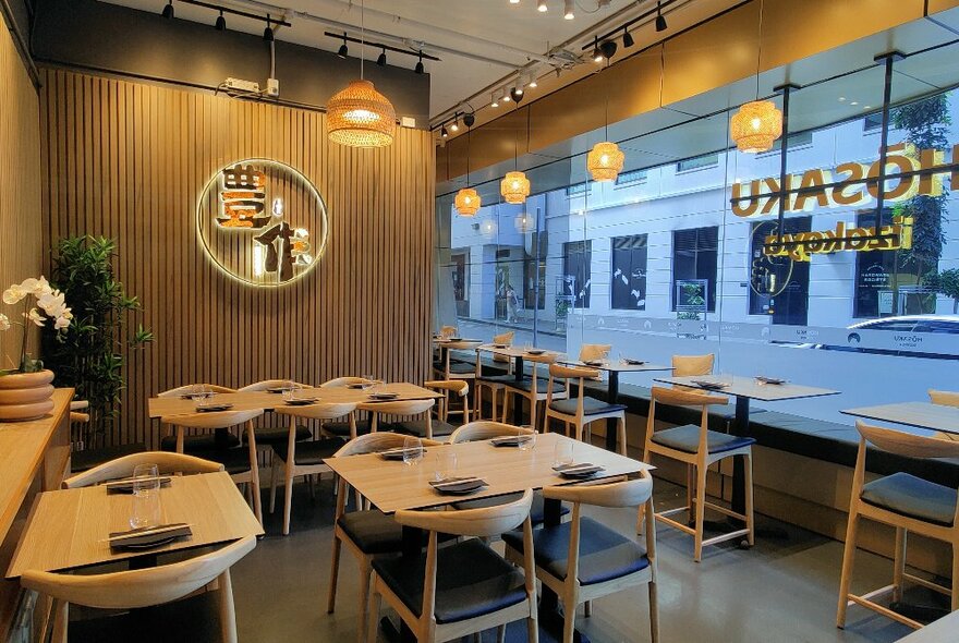 The empty dining room of a small restaurant with tables and chairs and a window looking out on the street. 