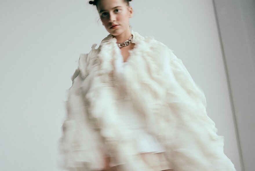 A fashion model wearing a white garment, slightly out of focus as if walking on a runway.