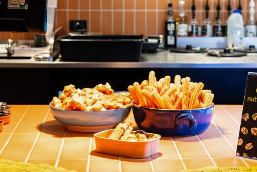 Dishes of Spanish doughnuts or churros on a counter in front of the food preparation area in a cafe.