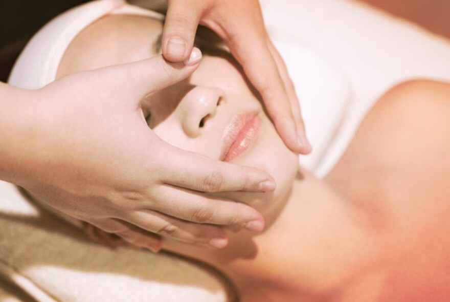 Woman lying on a bed receiving a face massage. 