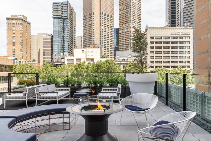 Rooftop terrace of the Lancemore Crossley St hotel, with outdoor furniture arranged around a small fire pit, city skyscrapers in the background.
