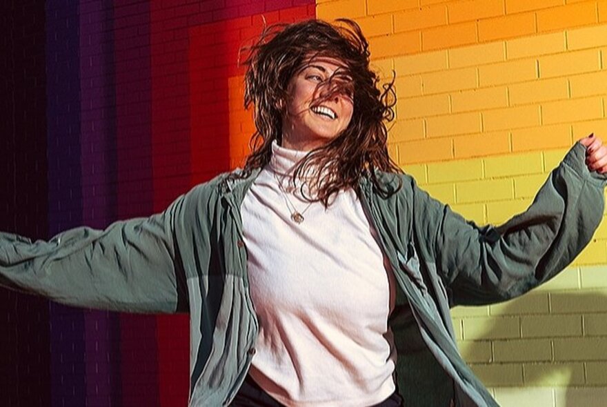A woman dancing in front of a rainbow-coloured brick wall.
