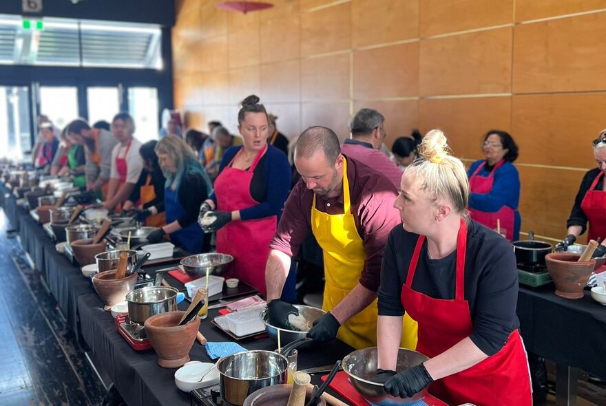 A group of people lined up at a black kitchen work bench with mortars and pestles and woks, participating in a Thai cooking class.