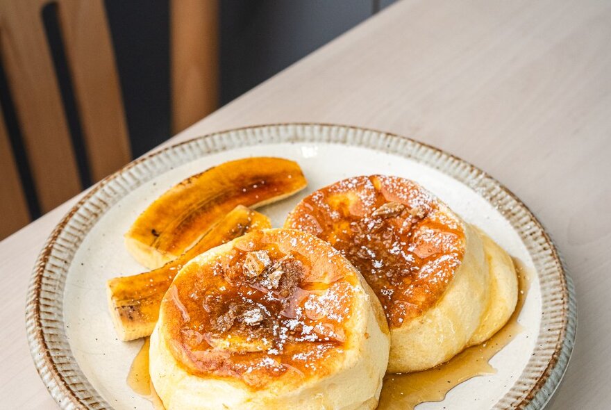 Soufflé pancakes on a plate with caramelised banana and syrup. 