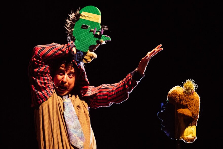 A puppeteer on stage with a green puppet made from recycled and found materials.