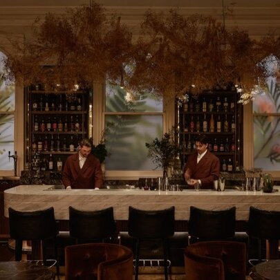 Five empty barstools at a luxury bar with two red-jacketed bartenders behind the bar.