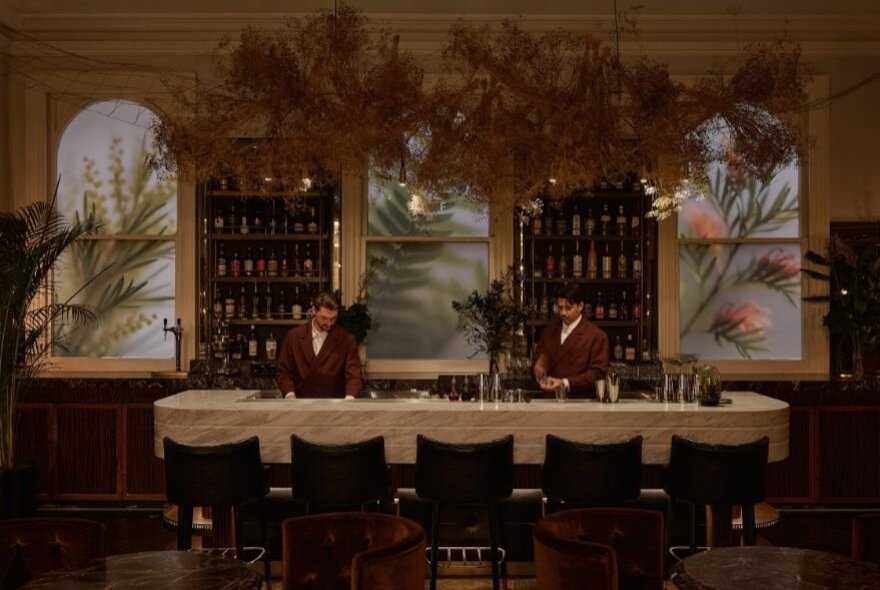Five empty barstools at a luxury bar with two red-jacketed bartenders behind the bar.