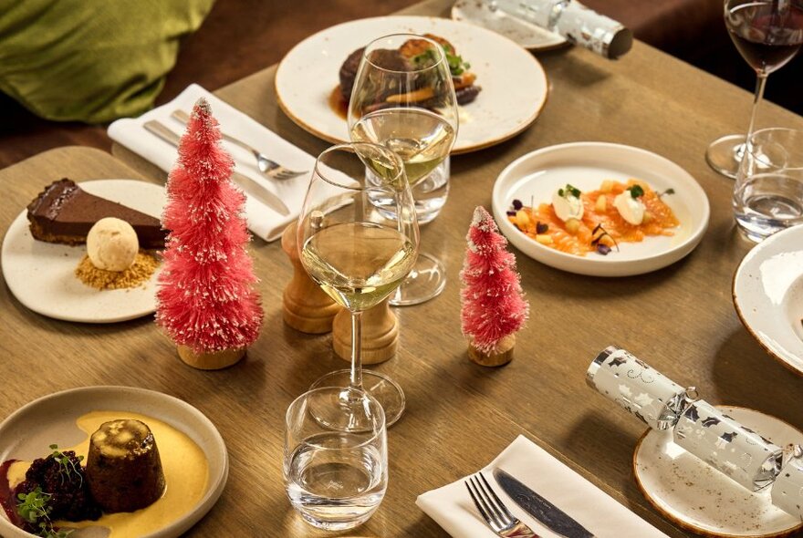 A table set for a festive Christmas lunch, with Christmas decorations, plates of dessert, white crockery, and wine glasses.