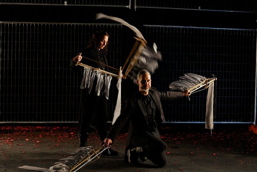 Musicians holding metal barsw with feathers in a dramatic setting.