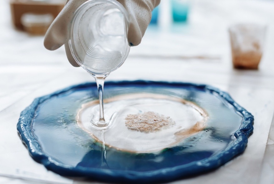 A hand pouring clear resin into a decorated plate.