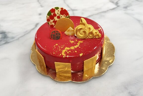 A celebration cake with Lunar New Year themed decorative pieces and a red and gold colour palette.