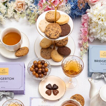 A selection of gourmet chocolates, biscuits and tea, seen from above on a table with floral decorations.