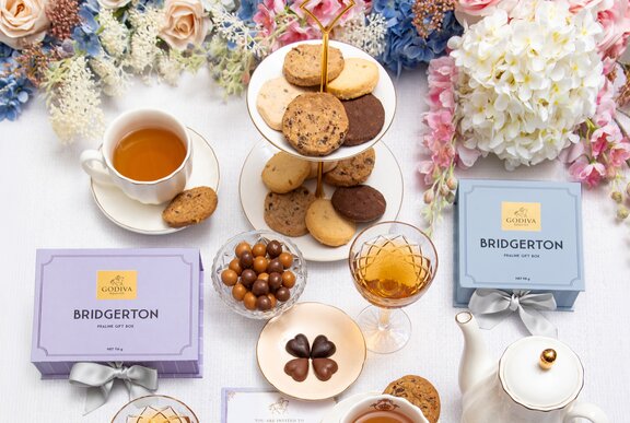 A selection of gourmet chocolates, biscuits and tea, seen from above on a table with floral decorations.