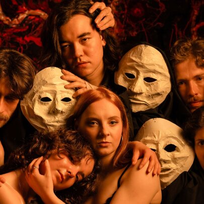 A theatre group posing for a picture with performers holding white face masks and hands on each other. 