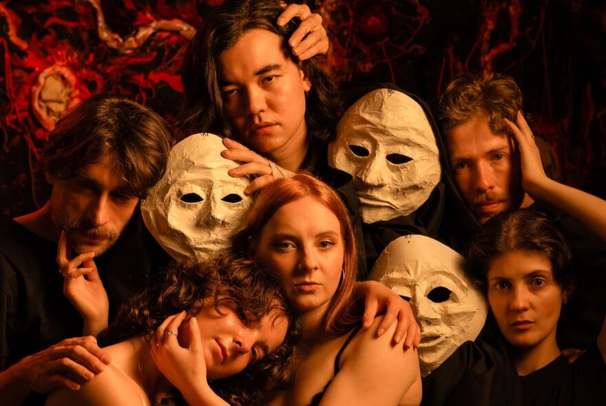 A theatre group posing for a picture with performers holding white face masks and hands on each other. 
