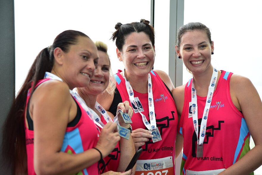 Four charity race participants wearing pink singlets holding lanyards around their necks.