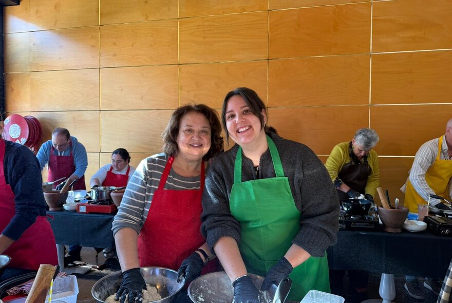 Two women in aprons, smiling at the camera as they participate in a Thai cooking class.