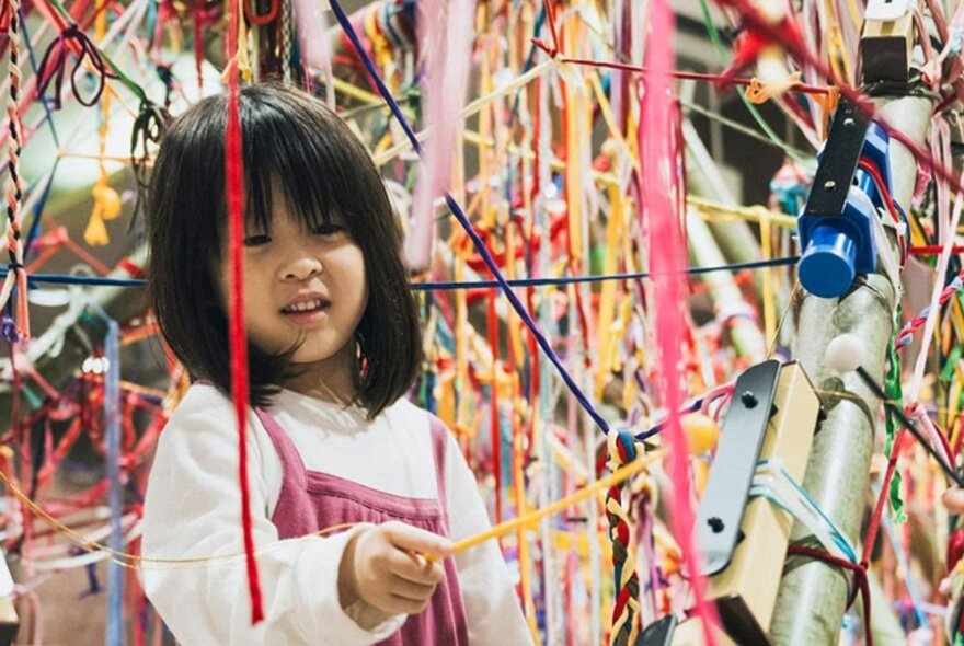 A young child amongst different colour wool and yarn that has been woven together to create a unique art installation.