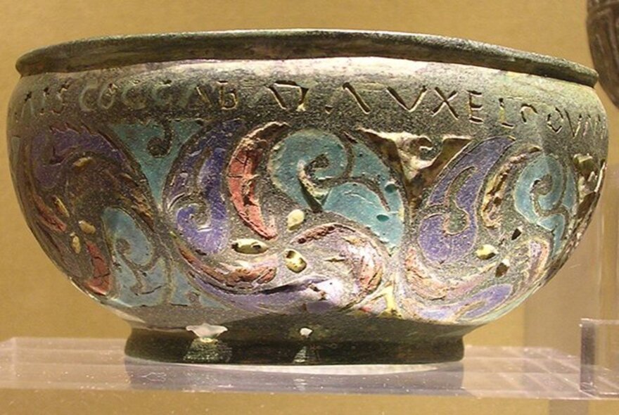An ancient Greek bowl with carving and painted decorations around the base. 