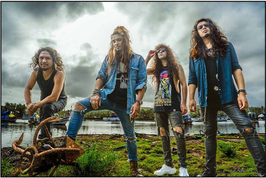 Rock band wearing ripped jeans and T-shirts, standing near waterway.