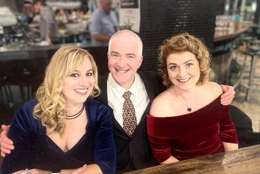 A man in the middle of two women, all dressed in formal clothes and smiling. 