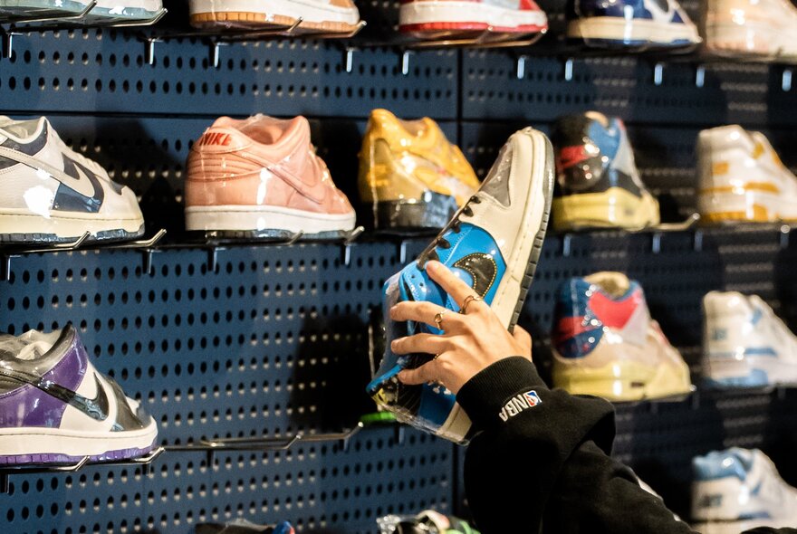 Hand holding a shoe from a wall display of sneakers.