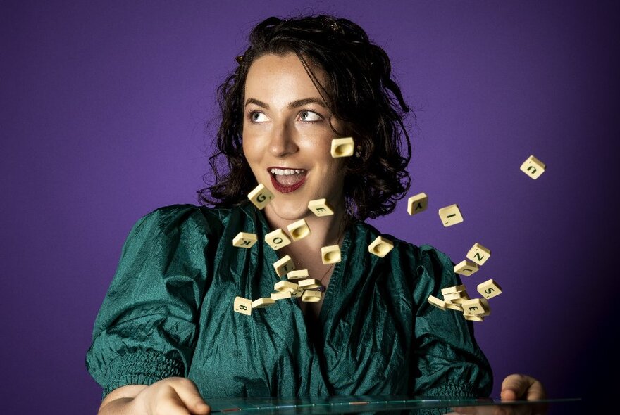 Woman with shoulder length hair, looking to her side, and throwing a selection of Scrabble letter tiles into the air.